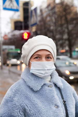 Portrait of elderly woman in winter clothes and mask during infectious diseaseの写真素材