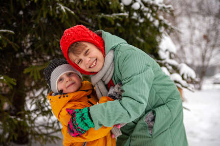 Portrait of two girls near snow - covered tree on walk in winter.