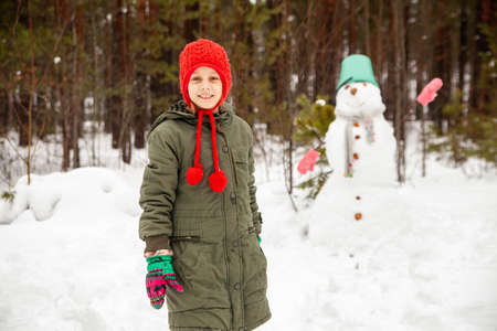 Girl in green coat in winter in forest near snowman.の写真素材