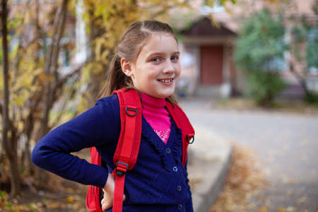 Portrait of elementary school student with red briefcase on autumn da