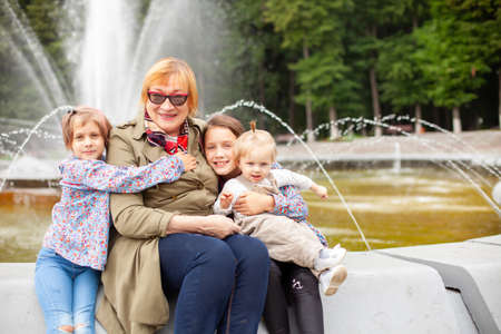 Portrait of 65-year-old woman with granddaughters on background of fountain in park