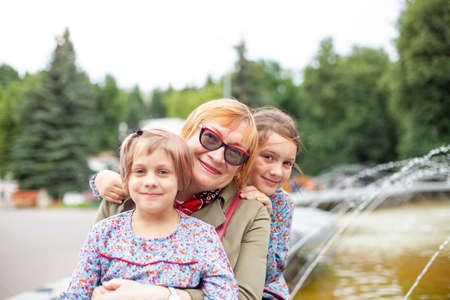 Portrait of 65-year-old woman with granddaughters on background of fountain in parkの写真素材