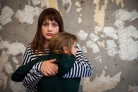 Two little girls standing in embrace at destroyed wall and afraid, concept of latest news in world about Russia's attack on Ukraineの写真素材