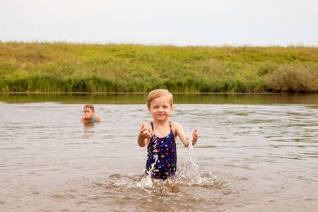 Adorable toddler girl wearing swimsuit and playing at river shore into water on hot sunny summer dayの写真素材