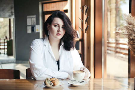Woman of plus size, American or European in coffee shop, young lady with excess weightの写真素材