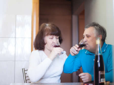 Senior man and woman with wine sitting next to each other in the kitchen.の写真素材