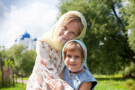 Portrait of older and younger sister in headscarves against the background of Orthodox churchの写真素材