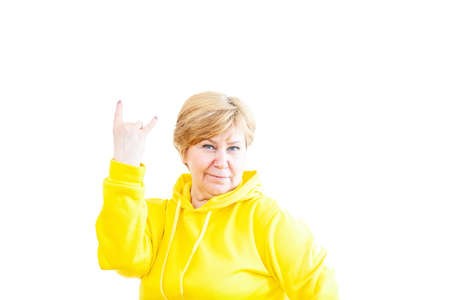 Fashionable elderly woman in sports hoodie showing rock sign on white background.