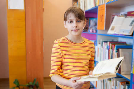 Child girl taking book from bookshelves in library, choosing.