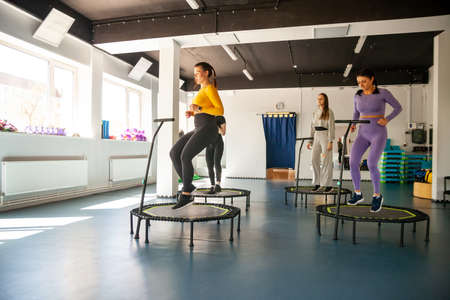 Group of happy women warming up before training in gym jumping on trampoline