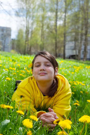 Portrait of teenage girl in yellow hoodie in spring meadow with dandelions.の写真素材