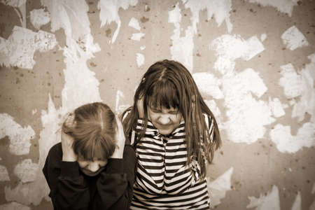 Two little girls standing in embrace at destroyed wall and afraid, concept of latest news in world...