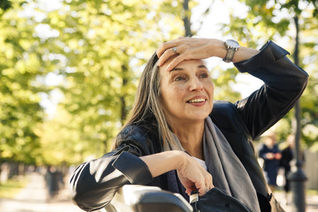 60-year-old woman sitting on bench and relaxing on autumn sunny day