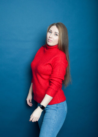 Young girl with long hair on a blue background in a red knitted sweaterの写真素材