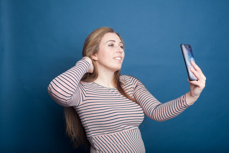Young plus size woman having fun looking at the screen of the phone. Positive laughing female selfie...