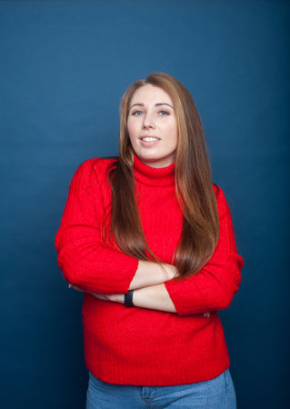 Young girl with long hair on a blue background in a red knitted sweater