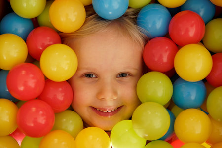 Smiling girl with colourful balls - colourful balls and girl playing with the balls. focus on mouth. Happy children playing and having fun at kindergarten with colourful balls. Happy girl with ballの写真素材