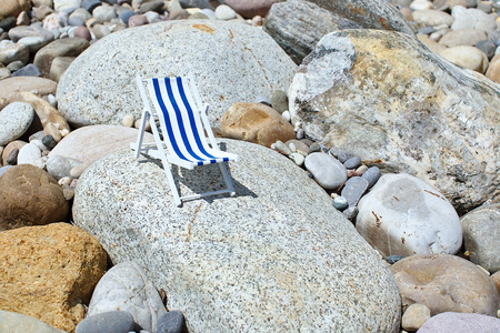 A toy striped beach chair for sunbathing and relaxing stands on a big stone on a sunny dayの写真素材