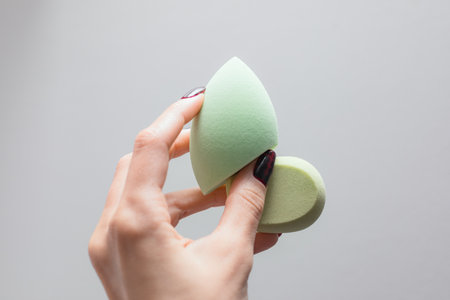 Girl's hand with dark manicure holds beauty sponge, beauty blender on white backgroundの写真素材