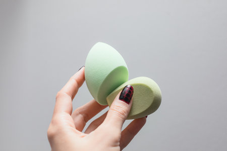 Girl's hand with dark manicure holds beauty sponge, beauty blender on white backgroundの写真素材