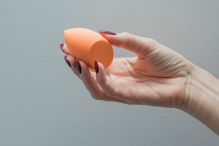 Girl's hand with dark manicure holds beauty sponge, beauty blender on white backgroundの写真素材