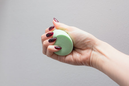 Girl's hand with dark manicure holds beauty sponge, beauty blender on white backgroundの写真素材