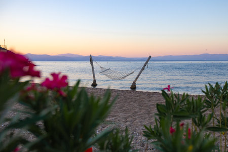 Hammock hanging in the water on the beach, no one nearby, calm sea, sunset and island in the backgroundの写真素材