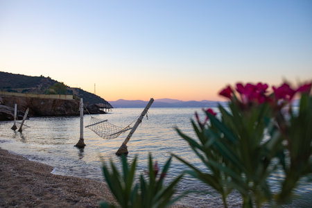 Hammock hanging in the water on the beach, no one nearby, calm sea, sunset and island in the backgroundの写真素材