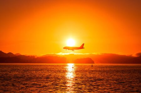 Airplane Flying Low Above Water by Sunsetの写真素材