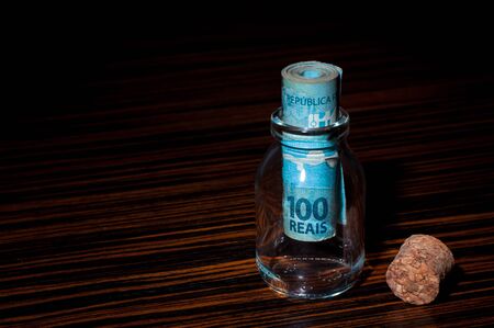 Roll of 100 Brazilian Reais Banknotes Inside a Small Glass Bottle, Saving Moneyの写真素材