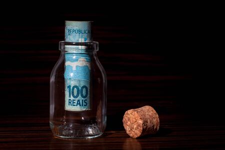 Roll of 100 Brazilian Reais Banknotes Inside a Small Glass Bottle, Saving Moneyの写真素材
