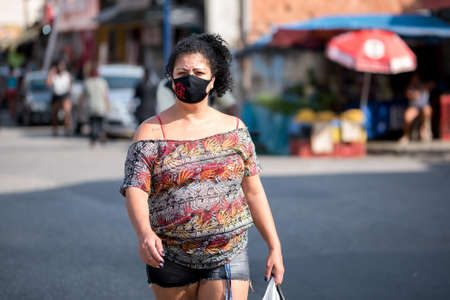 Rio de Janeiro, Brazil - July 3, 2020: People are wearing face masks during the Coronavirus pandemic in suburban area of the city. Woman crossing the street.のeditorial素材