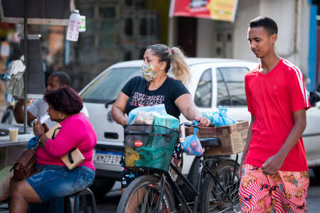 Rio de Janeiro, Brazil - July 3, 2020: Only some people are wearing face masks during the Coronavirus pandemic in suburban area of the city. Woman walking her bicycle with shopping bags.のeditorial素材