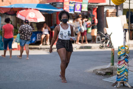 Rio de Janeiro, Brazil - July 3, 2020: People are wearing face masks during the Coronavirus pandemic in suburban area of the city. Woman with headphones crossing the street.のeditorial素材