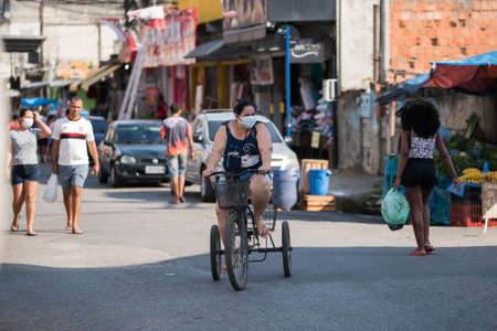 Rio de Janeiro, Brazil - July 3, 2020: People are wearing face masks during the Coronavirus pandemic in suburban area of the city. Woman on a tricycle among other people in the street.のeditorial素材
