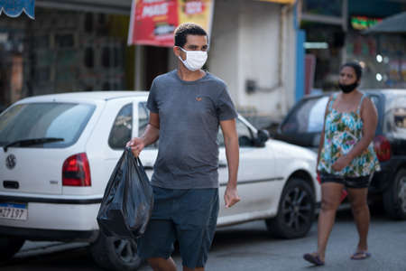 Rio de Janeiro, Brazil - July 3, 2020: People are wearing face masks during the Coronavirus pandemic in suburban area of the city. Man carrying black plastic bag.のeditorial素材
