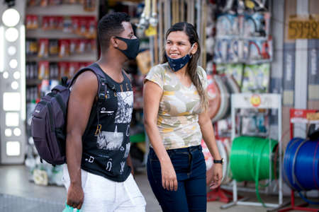 Rio de Janeiro, Brazil - July 3, 2020: People are wearing face masks during the Coronavirus pandemic in suburban area of the city. Man and woman walking ant talking.のeditorial素材