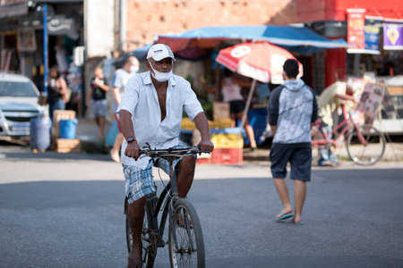 Rio de Janeiro, Brazil - July 3, 2020: People are wearing face masks during the Coronavirus pandemic in suburban area of the city. Elderly man on a bicycle in the street.のeditorial素材