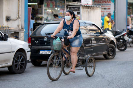 Rio de Janeiro, Brazil - July 3, 2020: People are wearing face masks during the Coronavirus pandemic in suburban area of the city. Woman with bags on a tricycle.のeditorial素材