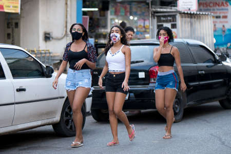Rio de Janeiro, Brazil - July 3, 2020: People are wearing face masks during the Coronavirus pandemic in suburban area of the city. Three young women walking down the street.のeditorial素材