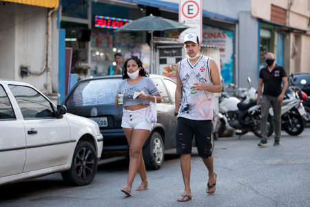Rio de Janeiro, Brazil - July 3, 2020: People are wearing face masks during the Coronavirus pandemic in suburban area of the city. Man and woman walking while having a snack.のeditorial素材