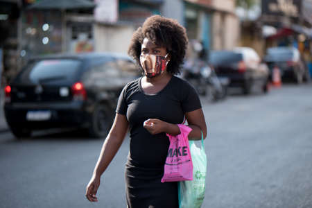 Rio de Janeiro, Brazil - July 3, 2020: People are wearing face masks during the Coronavirus pandemic in suburban area of the city. Woman carrying her bags on her hand.のeditorial素材
