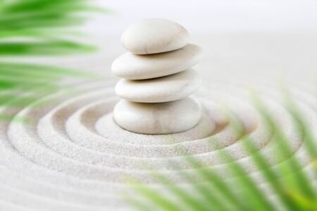 Stones pile in the sand behind palm leaves. Zen japanese gardenの写真素材