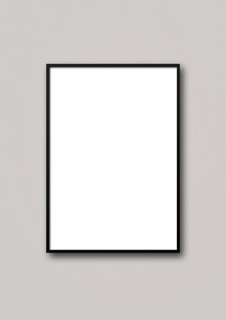 Black picture frame hanging on a light grey wall. Blank mockup templateの写真素材