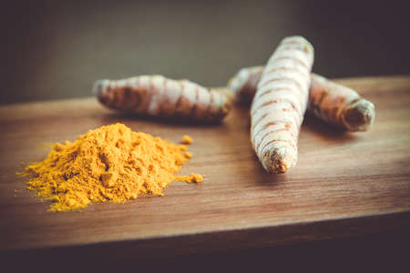 Turmeric root and spice powder on a wooden cutting boardの写真素材