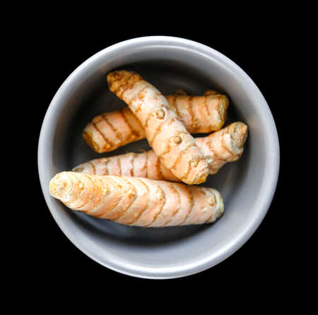 Turmeric root in a bowl isolated on black background. Top viewの写真素材