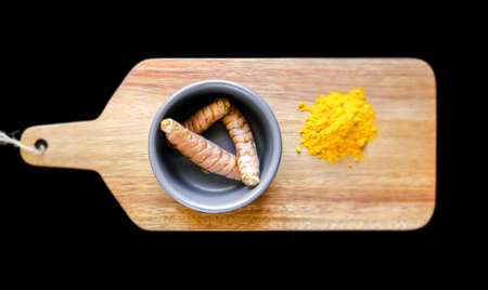 Turmeric root in bowl and spice powder on a wooden cutting board. Isolated on black backgroundの写真素材