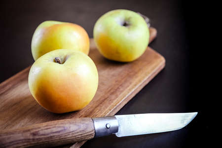 Organic fresh apples and pocket knife on a wooden cutting boardの写真素材