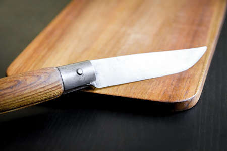 Wooden cutting board and pocket knife on a black kitchen table