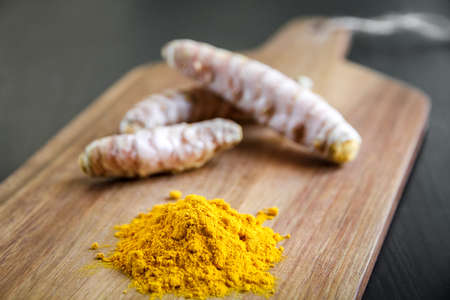 Turmeric root and spice powder on a wooden cutting board
